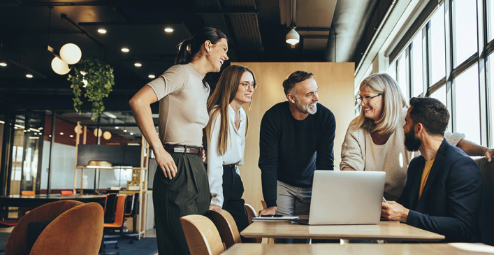 An image that shows group of people standing around a table in a workplace