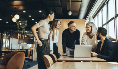 An image that shows group of people standing around a table in a workplace